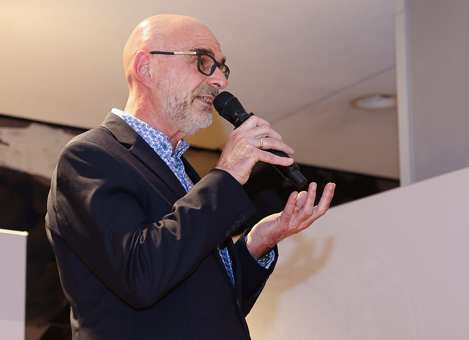 Axel Fell, ADFC NRW, Parlamentarischer Abend 2022 Der Landesvorsitzende des ADFC NRW, Axel Fell, spricht in ein Mikro. Er trägt ein gemustertes Hemd und ein schwarzes Sakko.